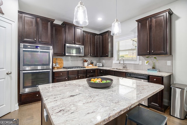 kitchen featuring a sink, dark brown cabinets, appliances with stainless steel finishes, light stone countertops, and tasteful backsplash