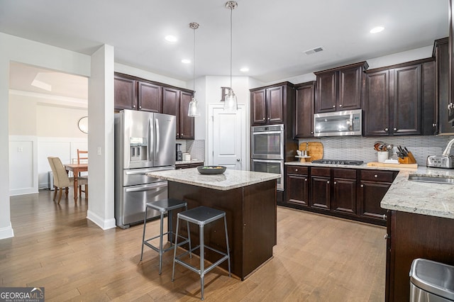 kitchen with light wood finished floors, visible vents, a kitchen island, appliances with stainless steel finishes, and dark brown cabinets