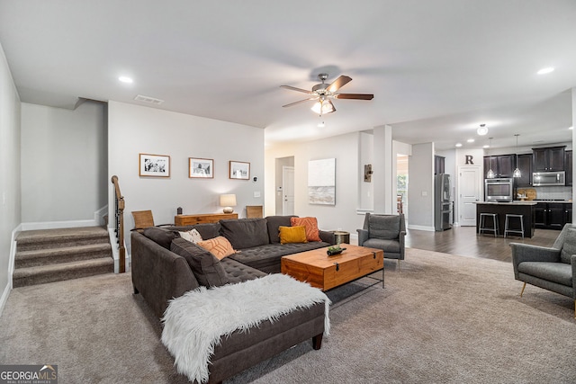 living room with stairs, ceiling fan, dark carpet, and visible vents