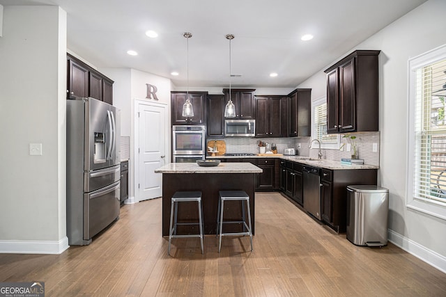 kitchen with stainless steel appliances, a sink, dark brown cabinets, a center island, and plenty of natural light