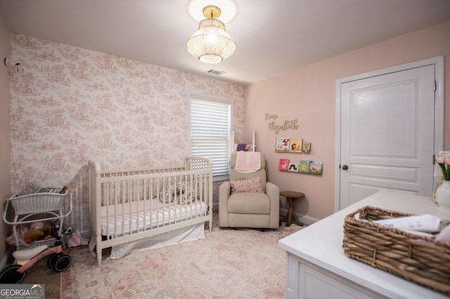 bedroom with visible vents, a crib, wallpapered walls, and baseboards