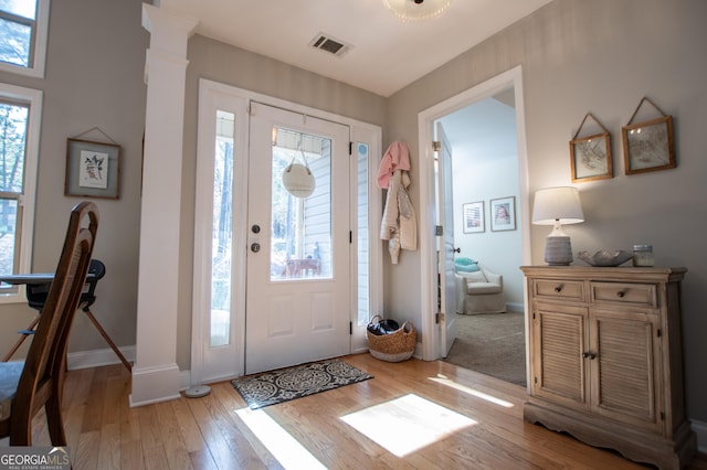 entrance foyer featuring ornate columns, visible vents, light wood-type flooring, and baseboards