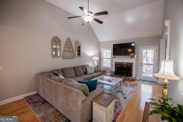 living room with ceiling fan, a brick fireplace, baseboards, and wood finished floors