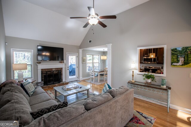 living room featuring high vaulted ceiling, ceiling fan, light wood-type flooring, and a fireplace