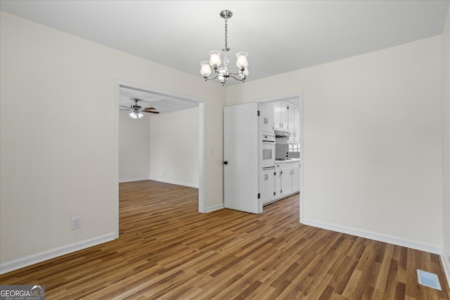 empty room featuring ceiling fan with notable chandelier and hardwood / wood-style floors