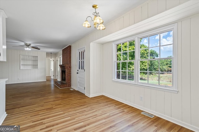 unfurnished living room featuring ceiling fan with notable chandelier, light hardwood / wood-style floors, and a fireplace