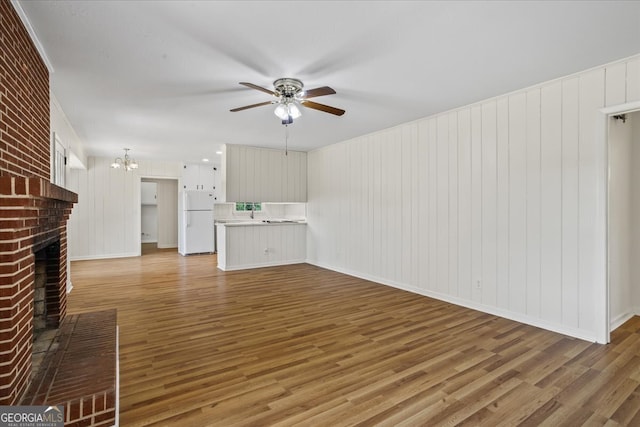 unfurnished living room with ceiling fan with notable chandelier, hardwood / wood-style flooring, a fireplace, and wood walls