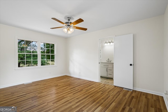 unfurnished bedroom featuring ceiling fan, hardwood / wood-style flooring, sink, and ensuite bathroom