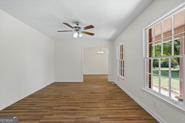 spare room featuring ceiling fan with notable chandelier and dark hardwood / wood-style flooring