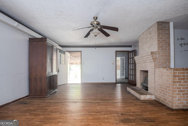 unfurnished living room with ceiling fan, dark hardwood / wood-style floors, a textured ceiling, and a brick fireplace