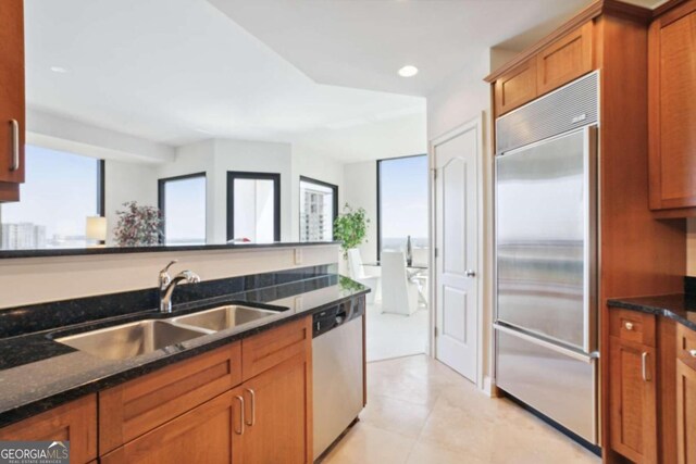 kitchen featuring a healthy amount of sunlight, appliances with stainless steel finishes, dark stone counters, and sink