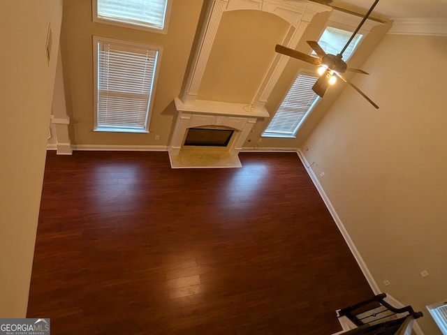 unfurnished living room featuring ceiling fan, crown molding, a towering ceiling, dark wood-type flooring, and a fireplace