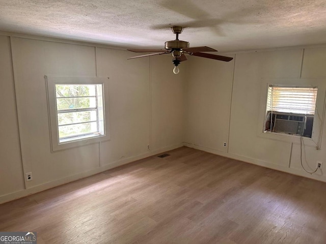 empty room featuring light hardwood / wood-style floors, cooling unit, a textured ceiling, and ceiling fan