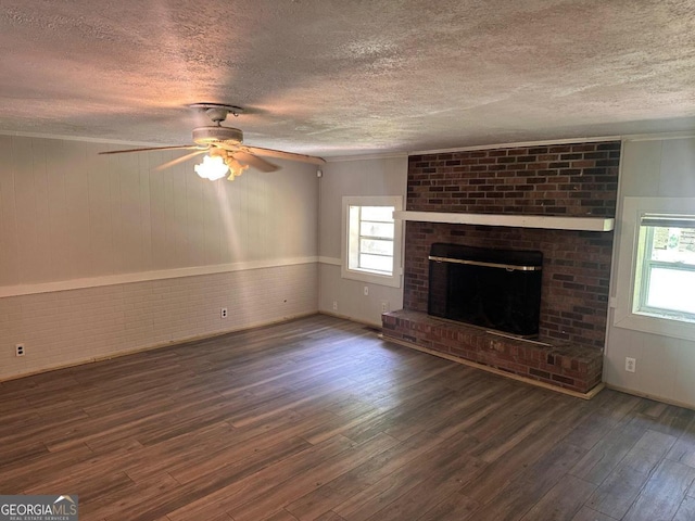 unfurnished living room with ceiling fan, a textured ceiling, a brick fireplace, dark wood-type flooring, and wooden walls