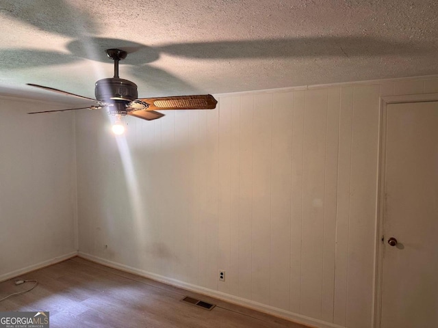 interior space featuring wood walls, a textured ceiling, wood-type flooring, and ceiling fan