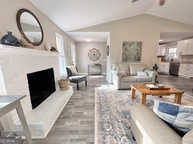 living room featuring plenty of natural light, vaulted ceiling, sink, and light hardwood / wood-style flooring