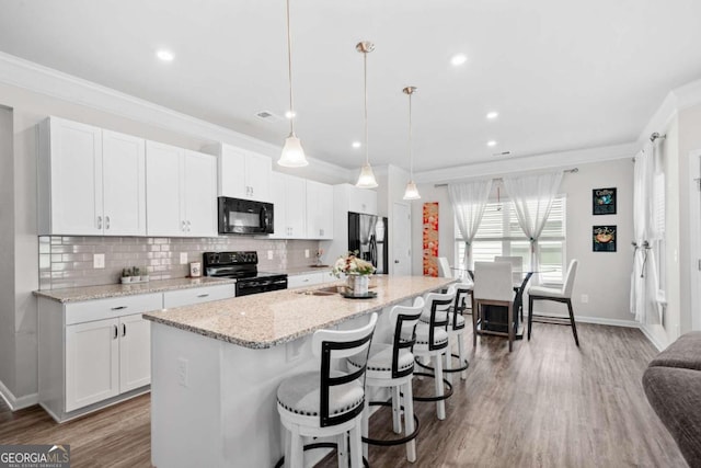 kitchen with pendant lighting, white cabinetry, a kitchen island with sink, black appliances, and decorative backsplash