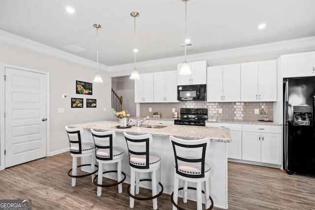 kitchen with white cabinetry, hanging light fixtures, black appliances, and a kitchen island with sink