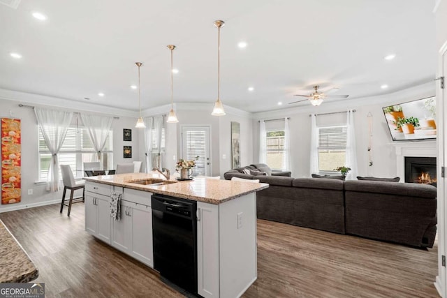 kitchen with hanging light fixtures, white cabinets, light stone countertops, black dishwasher, and an island with sink