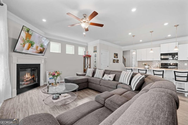 living room featuring light hardwood / wood-style flooring, ceiling fan, and ornamental molding