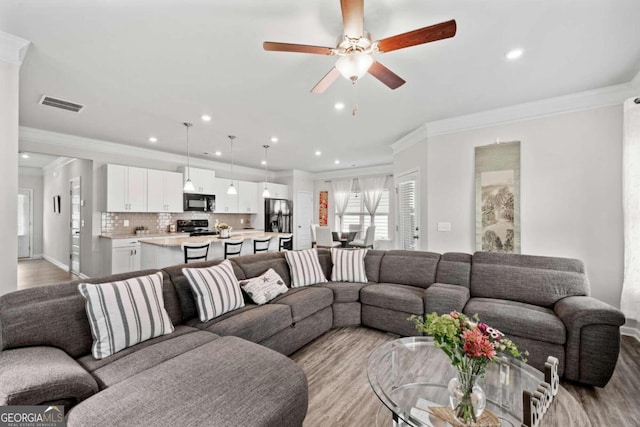 living room with ceiling fan, ornamental molding, and light wood-type flooring