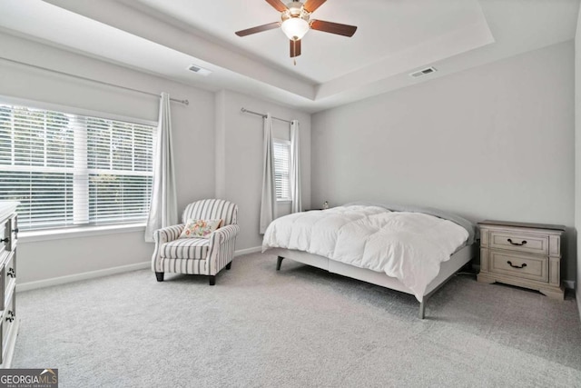 carpeted bedroom with multiple windows, a tray ceiling, and ceiling fan