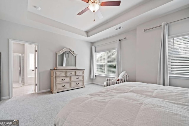 bedroom with ceiling fan, ensuite bathroom, a raised ceiling, and light colored carpet