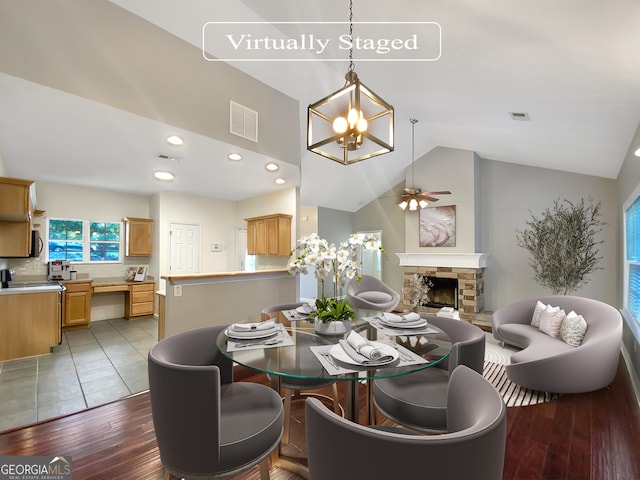 dining room featuring high vaulted ceiling, ceiling fan with notable chandelier, a stone fireplace, and light wood-type flooring