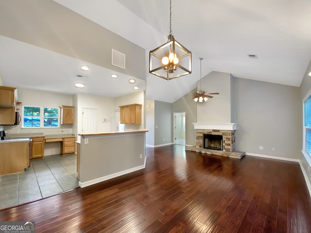 kitchen featuring ceiling fan with notable chandelier, hardwood / wood-style floors, decorative light fixtures, and a stone fireplace