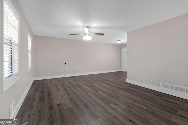 empty room with dark wood-type flooring, ceiling fan, and a healthy amount of sunlight