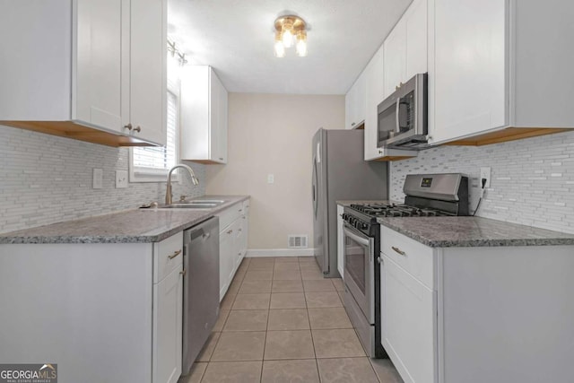 kitchen featuring backsplash, light tile patterned floors, stainless steel appliances, sink, and white cabinets