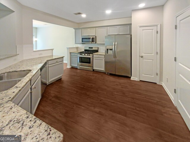 kitchen with gray cabinets, appliances with stainless steel finishes, light stone counters, and dark wood-type flooring