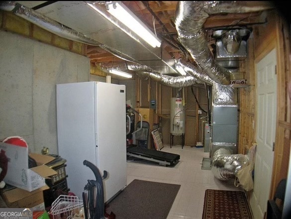 basement with strapped water heater, white refrigerator, and heating unit