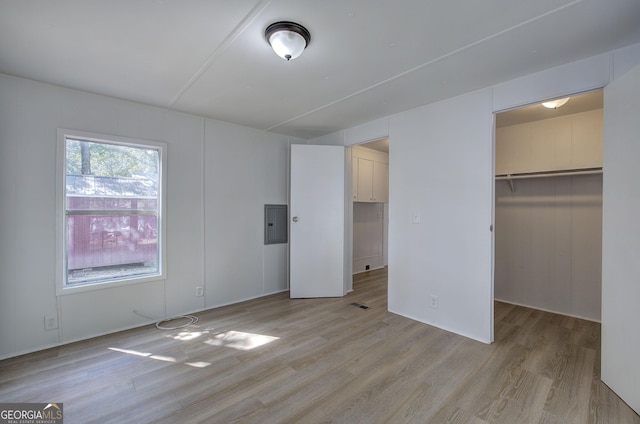 unfurnished bedroom with light wood finished floors, visible vents, a walk in closet, electric panel, and a closet