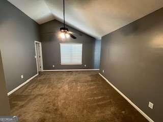 empty room featuring vaulted ceiling, dark colored carpet, and ceiling fan