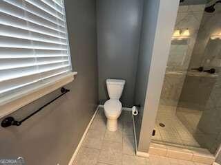 bathroom featuring toilet, tile patterned floors, and a tile shower