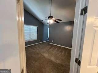 spare room featuring vaulted ceiling, dark carpet, and ceiling fan