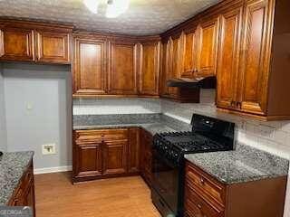 kitchen featuring light wood-type flooring, dark stone counters, black gas range, and backsplash