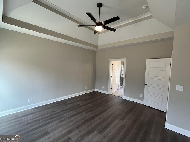 empty room with a tray ceiling, dark wood-type flooring, and ceiling fan