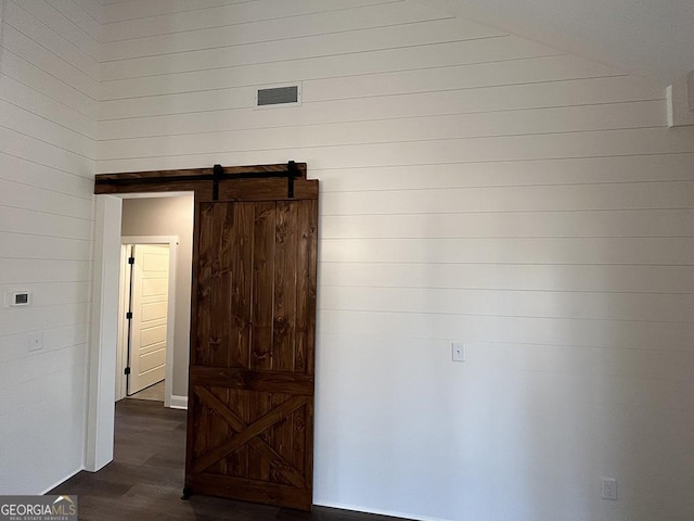 empty room with a barn door, wooden walls, and dark hardwood / wood-style flooring