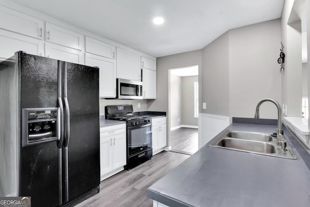 kitchen with baseboards, light wood-style flooring, black appliances, white cabinetry, and a sink