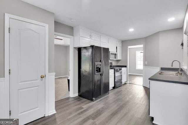 kitchen with range with gas cooktop, stainless steel microwave, black fridge with ice dispenser, white cabinetry, and a sink