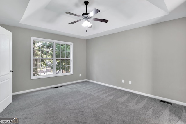 empty room with carpet floors, visible vents, a tray ceiling, and baseboards