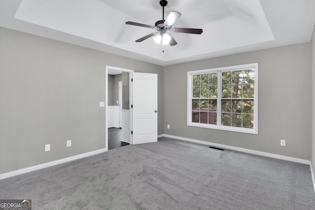 unfurnished bedroom featuring a tray ceiling, dark colored carpet, visible vents, ceiling fan, and baseboards