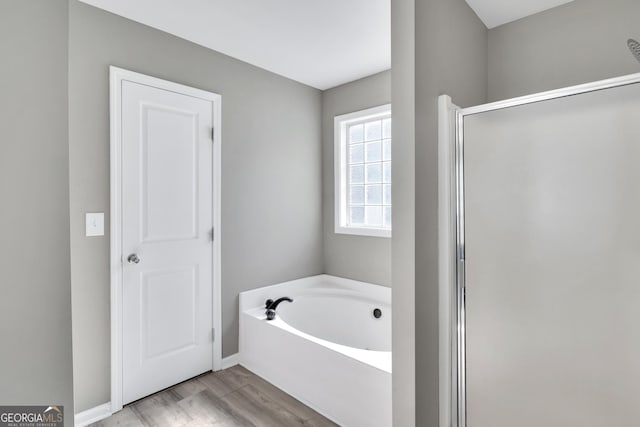 full bathroom featuring baseboards, wood finished floors, a bath, and a shower stall