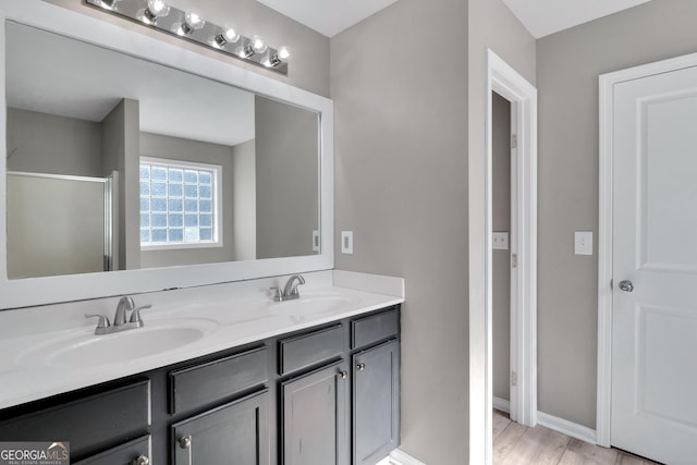 full bathroom featuring double vanity, a shower with door, a sink, and wood finished floors