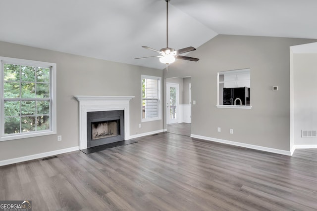 unfurnished living room with baseboards, visible vents, a fireplace with raised hearth, lofted ceiling, and wood finished floors