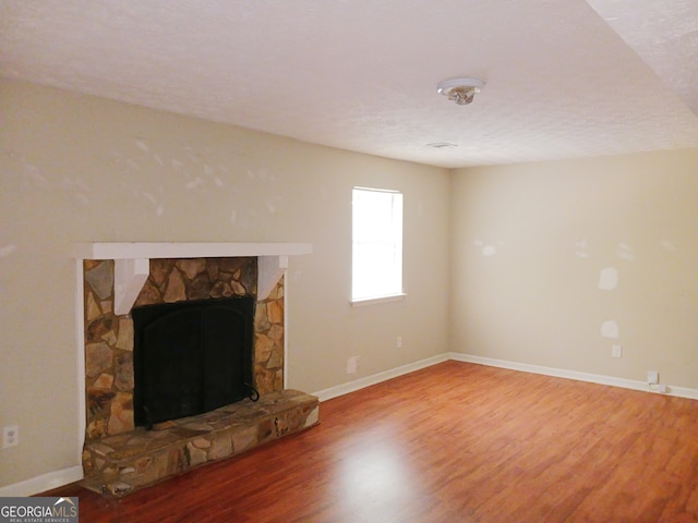 living room with a textured ceiling, wood-type flooring, and a stone fireplace