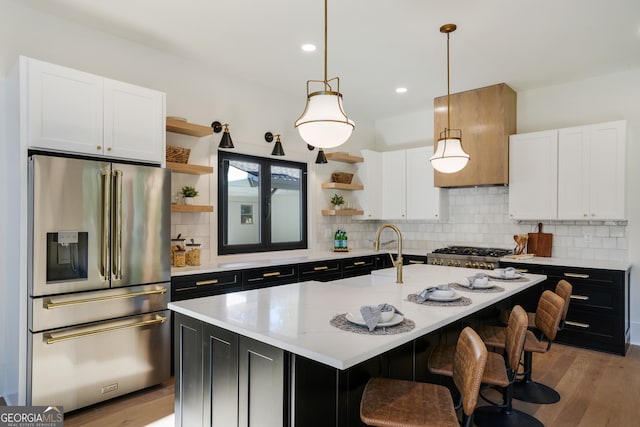 kitchen with a center island with sink, decorative light fixtures, light hardwood / wood-style floors, white cabinetry, and stainless steel appliances