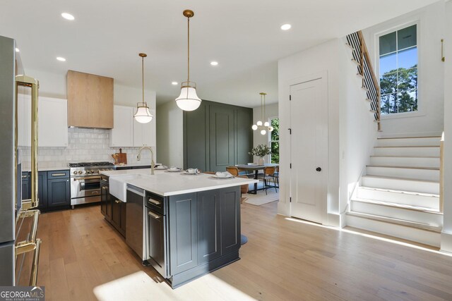 kitchen with a kitchen island with sink, sink, hanging light fixtures, light wood-type flooring, and appliances with stainless steel finishes